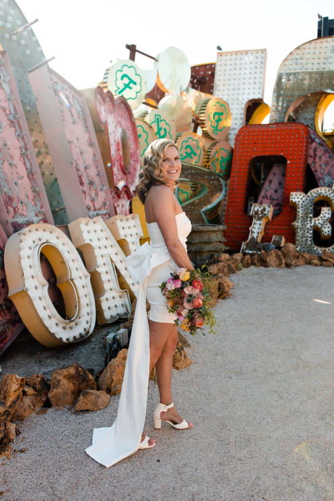 A bride in a short dress with a bow on the back at the Neon Museum