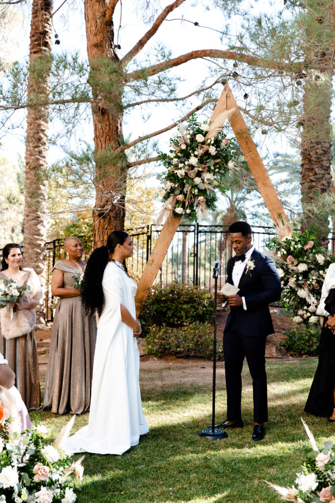 Bride and groom at alter with triangle, wooden arbor and neutral floral arrangement.