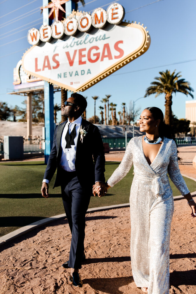Bride in sequin jumpsuit and groom at welcome to Las Vegas sign