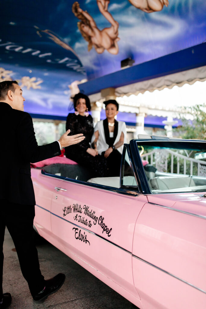 The brides sit in the backseat of the iconic pink Cadillac at A Little White Chapel, ready to drive off and start their new life together.