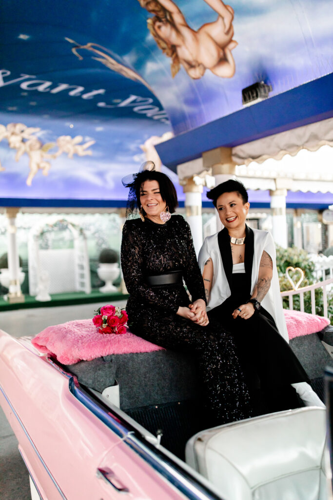 Two brides share a loving embrace in front of A Little White Chapel, radiating happiness on their special day.