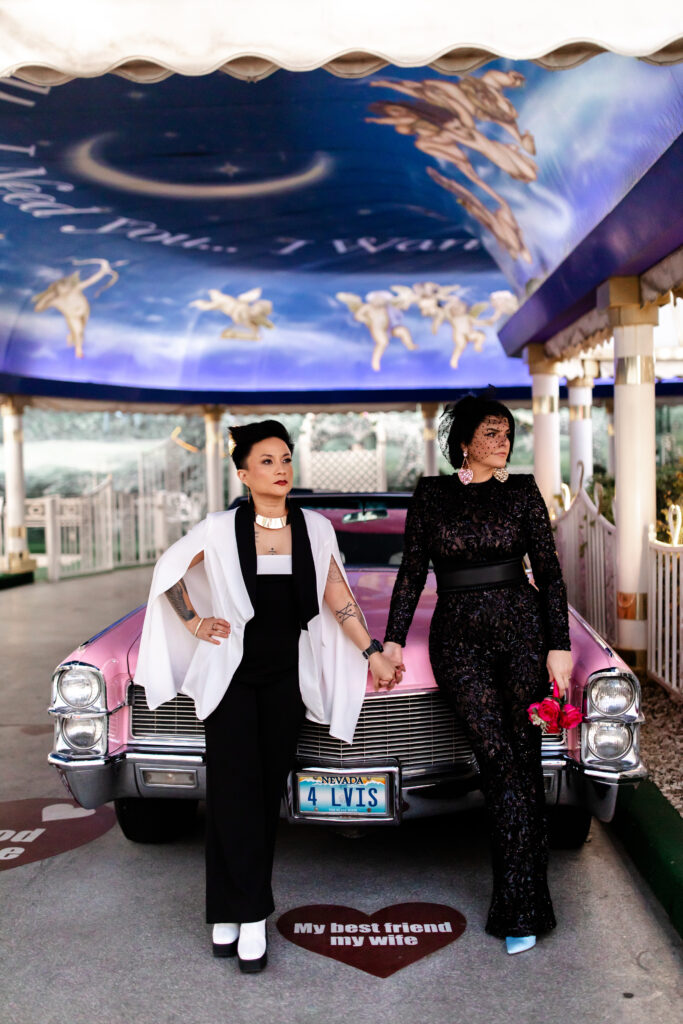 The brides pose next to a classic pink Cadillac, adding a touch of nostalgia to their special day at A Little White Chapel.