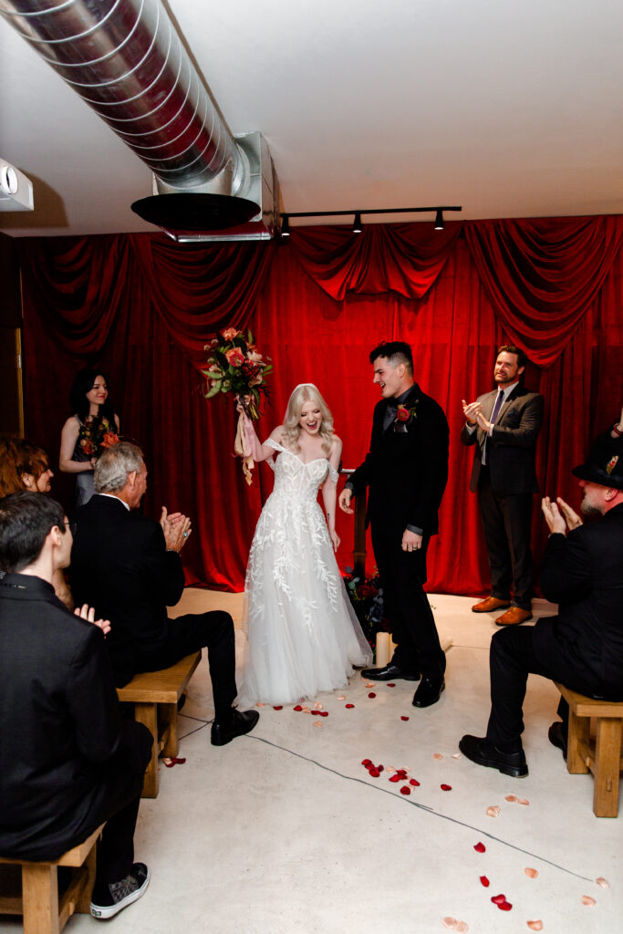 The newlyweds walk back down the aisle, surrounded by clapping and cheering friends and family, celebrating their union in the unique setting of the Punk Rock Museum.