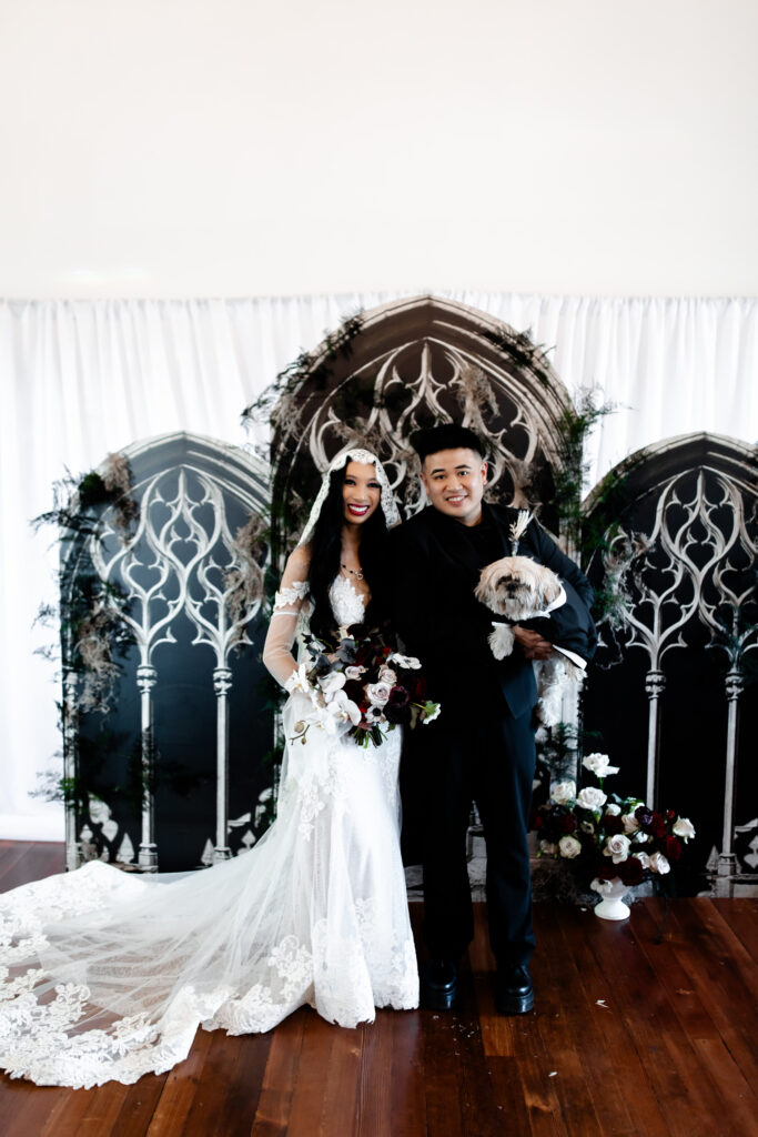 The bride and groom pose with their beloved dog at the Sonic Temple, capturing a heartwarming family moment on their special day.