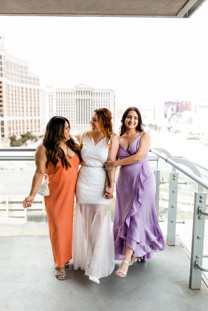 The bridesmaids gather on the balcony of the Cosmopolitan suite wearing bright colored dresses, sharing laughter and joy as they celebrate the special day.