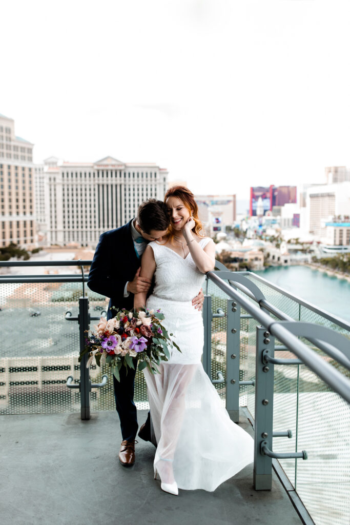 The bride and groom pose for a portrait on the balcony, with the luxurious backdrop of the Cosmopolitan suite and cityscape.