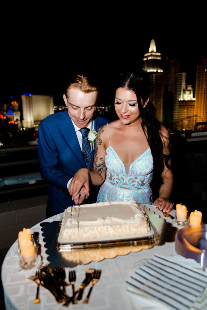 The bride and groom cut their elegantly decorated wedding cake on the terrace of their MGM Grand suite, with the Las Vegas skyline twinkling behind them.