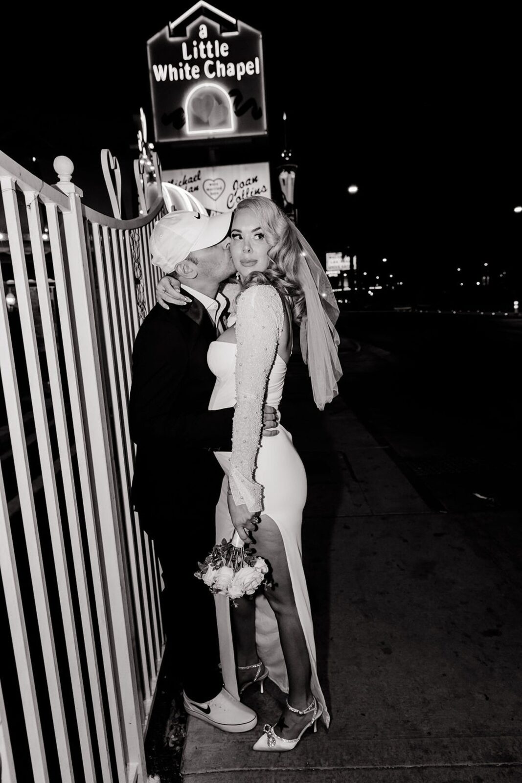 Black and white photo of a groom kissing his bride on the cheek during their editorial Vegas elopement at Little White Wedding Chapel