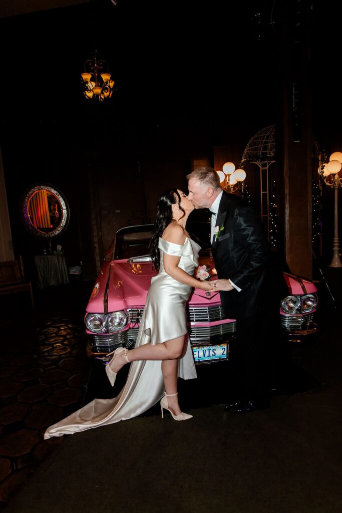 Bride and groom kissing in front of the Pink Cadillac at Viva Las Vegas wedding Chapel