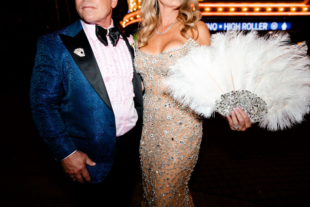 Close-up detail of the bride’s feather fan and crystal-embellished gown paired with the groom’s textured blue suit