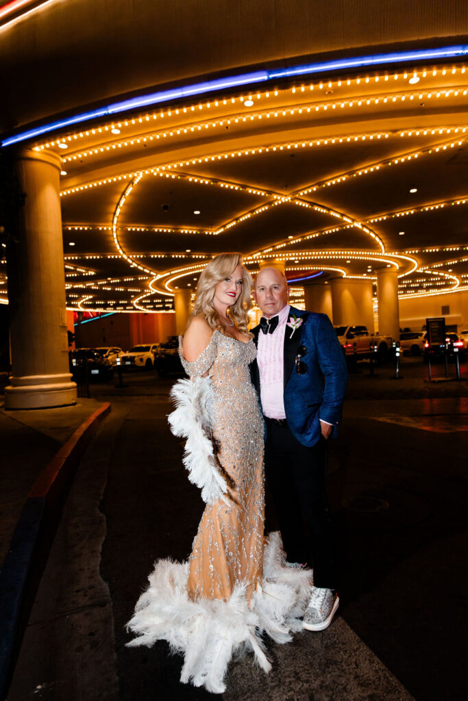 Couple poses confidently together under the neon canopy outside the Flamingo, with the bride holding a dramatic feather fan