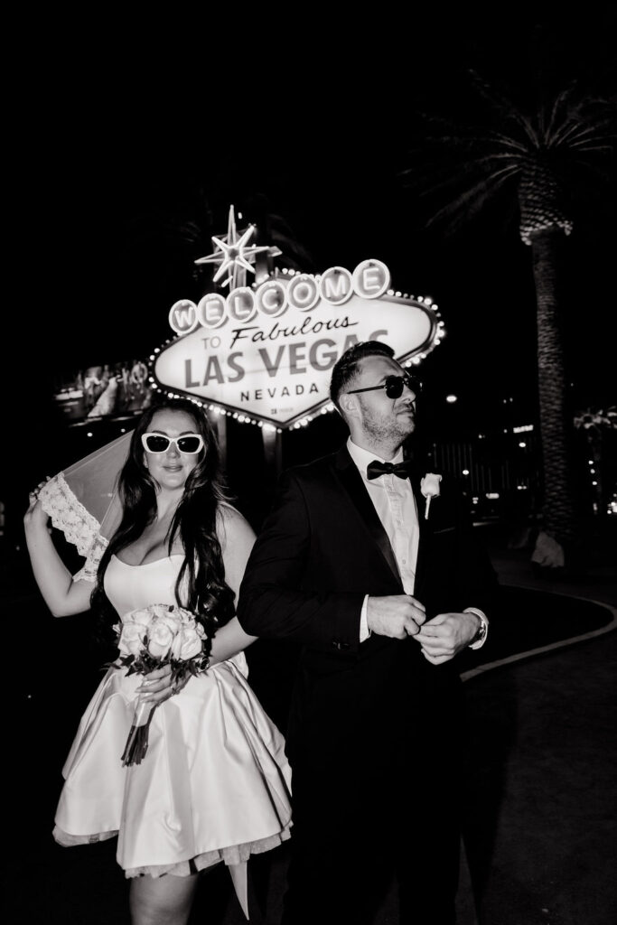 Black and white photo of a bride and groom posing in front of the Welcome to Fabulous Las Vegas sign