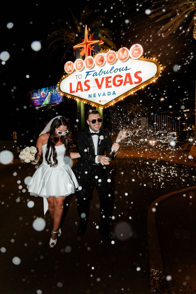 Couple popping champagne in front of the the Welcome to Fabulous Las Vegas sign at night