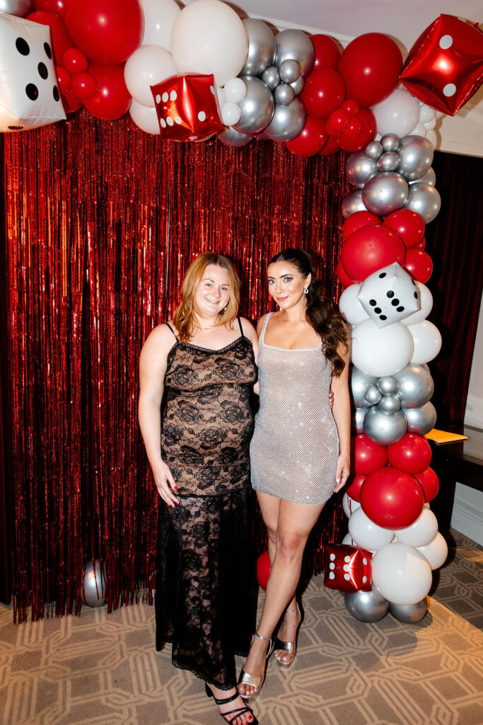 Bride in silver mini dress and her friend in a black lace gown posing at a Lucky in Love bachelorette party in Las Vegas