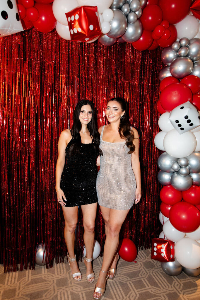 Bride in silver dress smiling with her friend in a glittery black dress at a Lucky in Love bachelorette celebration in Las Vegas