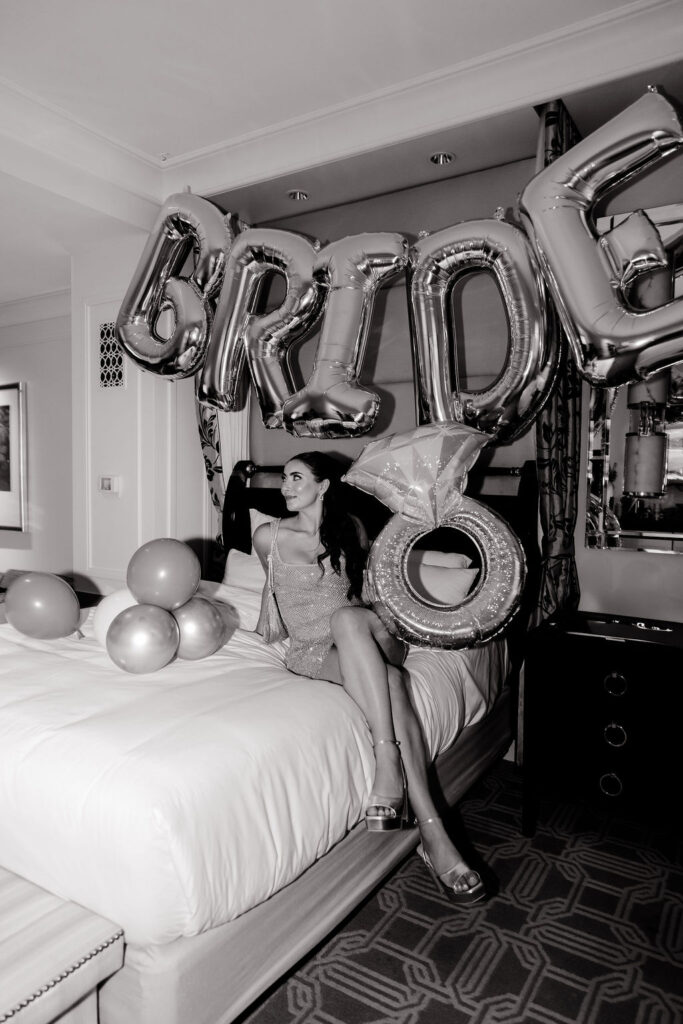 Bride lounging on hotel bed with silver ‘BRIDE’ balloons and diamond ring balloon at her Las Vegas Lucky in Love bachelorette party