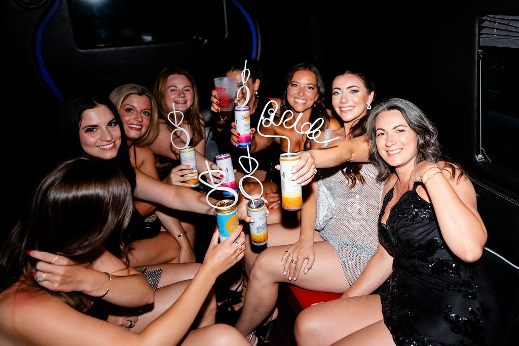 Bride and her bridal party smiling and holding up custom curly straws and drinks while celebrating together in a Las Vegas limo