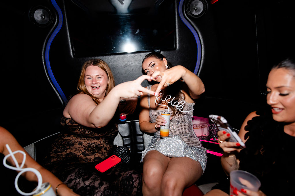 Bride and bridesmaid making a heart with their hands while laughing together in a Las Vegas party bus.