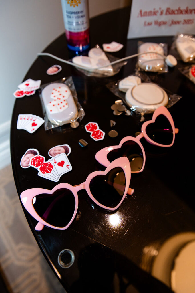 Pink heart sunglasses, casino-themed cookies, and playful Lucky in Love bachelorette party favors laid out in a Las Vegas hotel suite