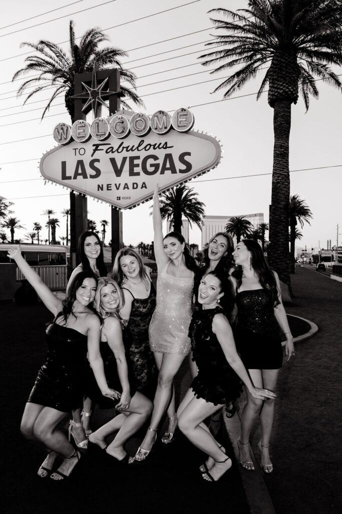 Black and white photo of bride and her bridal party celebrating at the Welcome to Fabulous Las Vegas sign