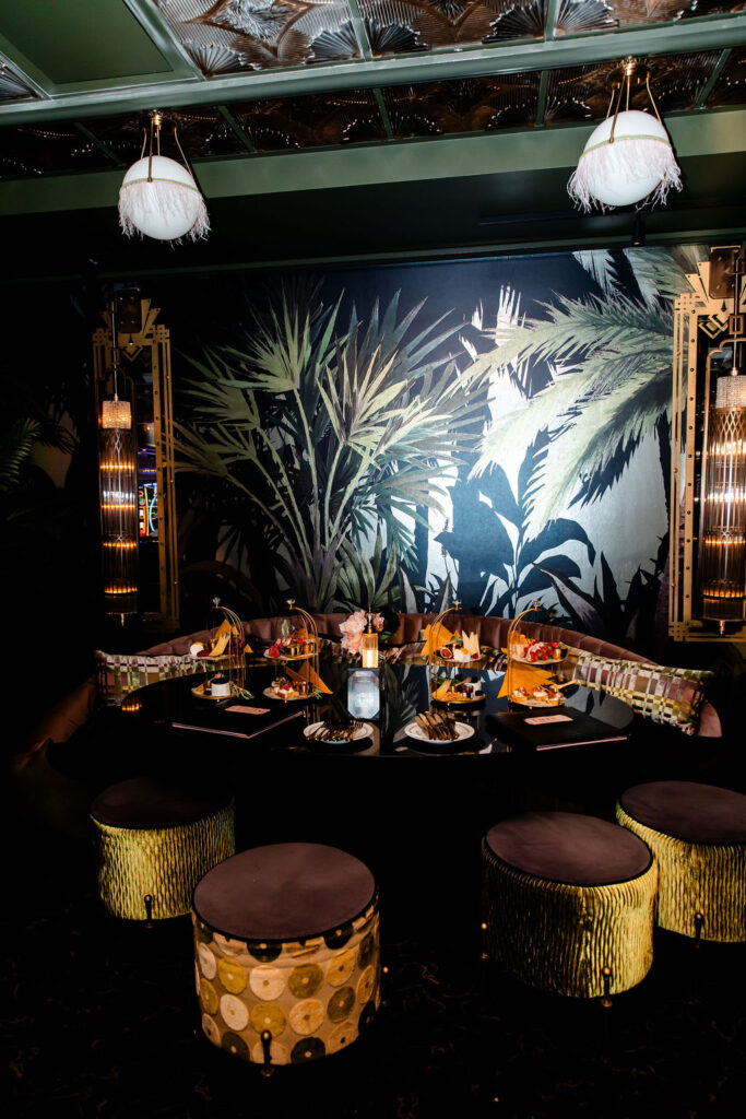 Moody reception setup at Pinky’s by Vanderpump with tropical wallpaper and velvet seating.