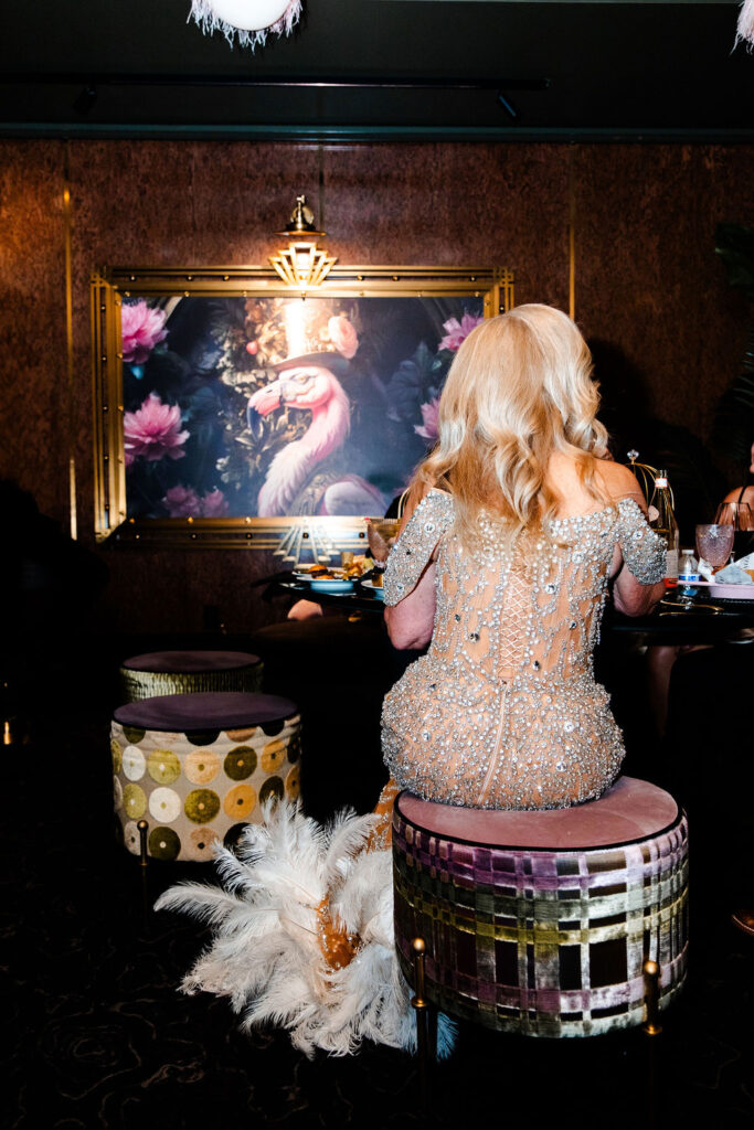 Bride seated in sparkling gown with feather detail, captured against flamingo wall art at Pinky’s Vanderpump Las Vegas wedding reception.
