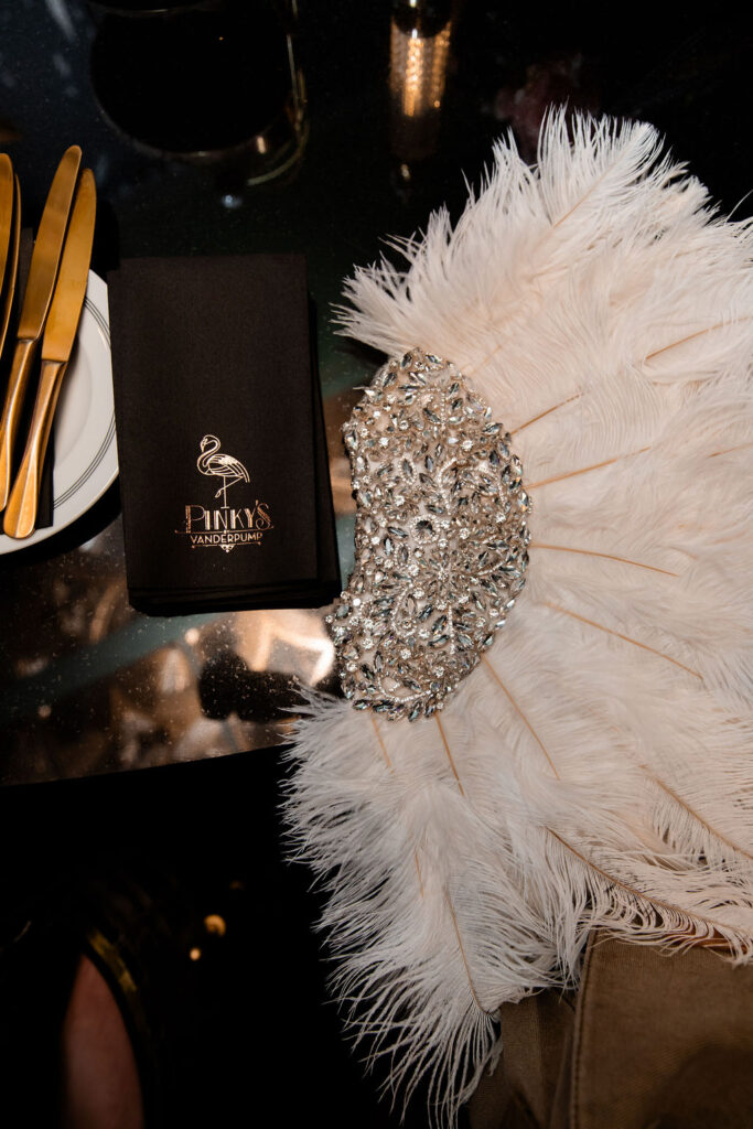 Feather fan and rhinestone detail with Pinky’s Las Vegas napkin on reception table.