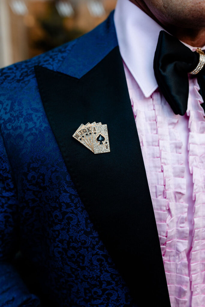 Navy patterned jacket with a jeweled playing card lapel pin and pink ruffled shirt at a Las Vegas wedding.