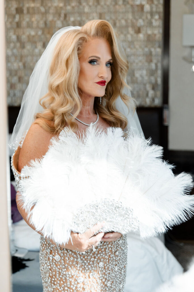 A bride holds a glamorous white feather fan while wearing a crystal gown and veil during portraits at Waldorf Astoria