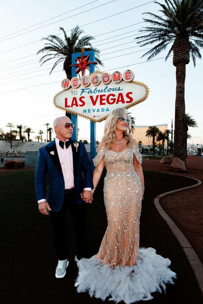 A couple in chic Vegas wedding attire strolls beneath the iconic Welcome to Fabulous Las Vegas sign.