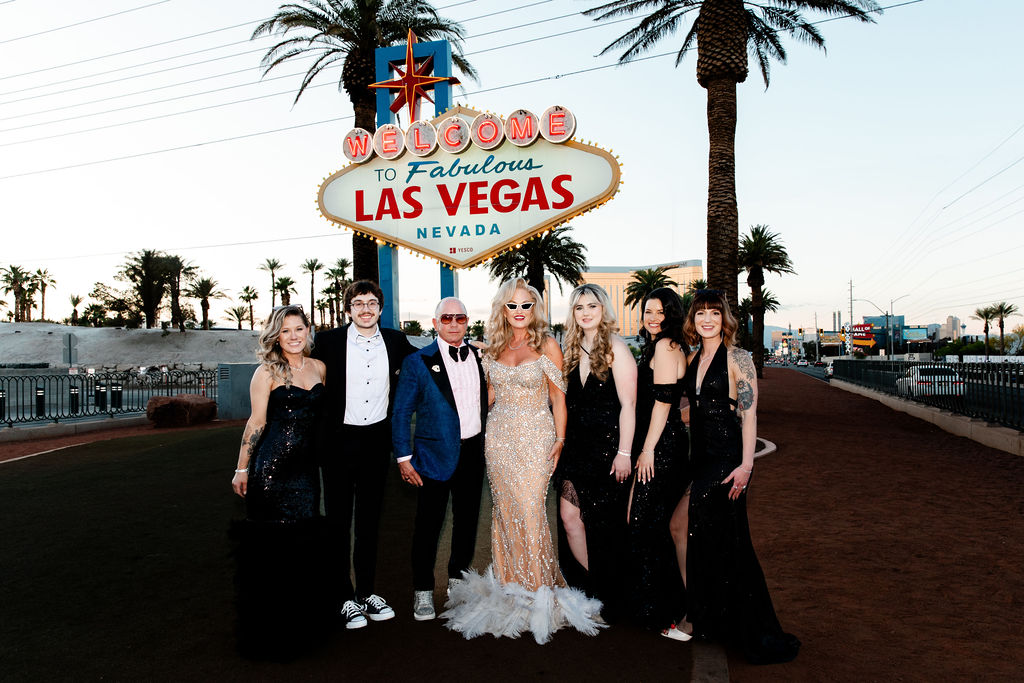 The couple poses with their wedding party dressed in sleek black outfits under the Welcome to Fabulous Las Vegas sign