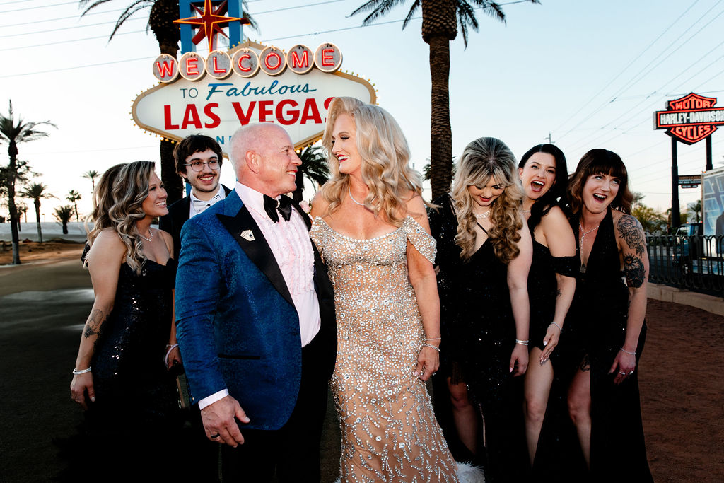 The couple laughs with their wedding party in front of the iconic sign, creating playful, candid Vegas wedding photos.
