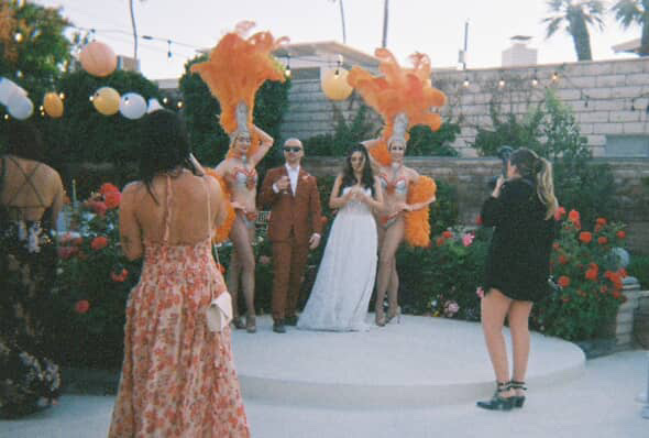 Las Vegas wedding photographer taking a photo of the bride and groom posing with the showgirls at Mid Century Manor in Las Vegas