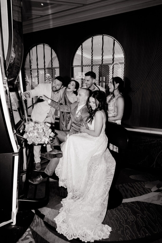 Black and white photo of a bride and groom playing the slots with their wedding party at Bellagio