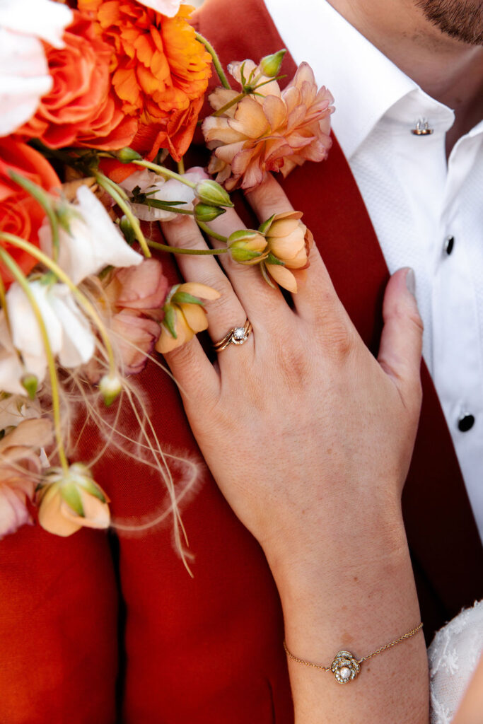 Close up shot of a bride resting her hand on her grooms chest and showing off her wedding ring and colorful spring wedding bouquet by Mylo Fleur