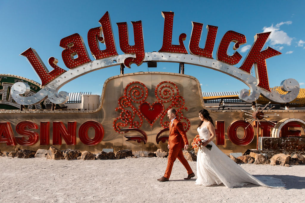 Bride and groom walking in front of the Lady Luck sign at Neon Museum in Las Vegas