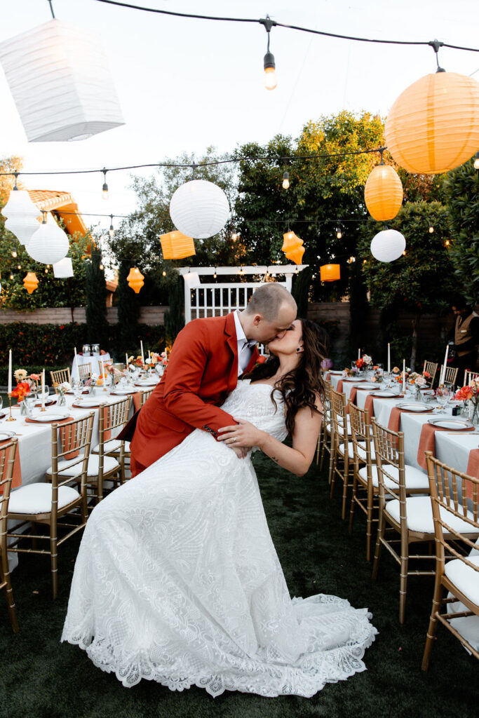 Couple kissing between reception tables decorated with lanterns and florals at Mid Century Manor