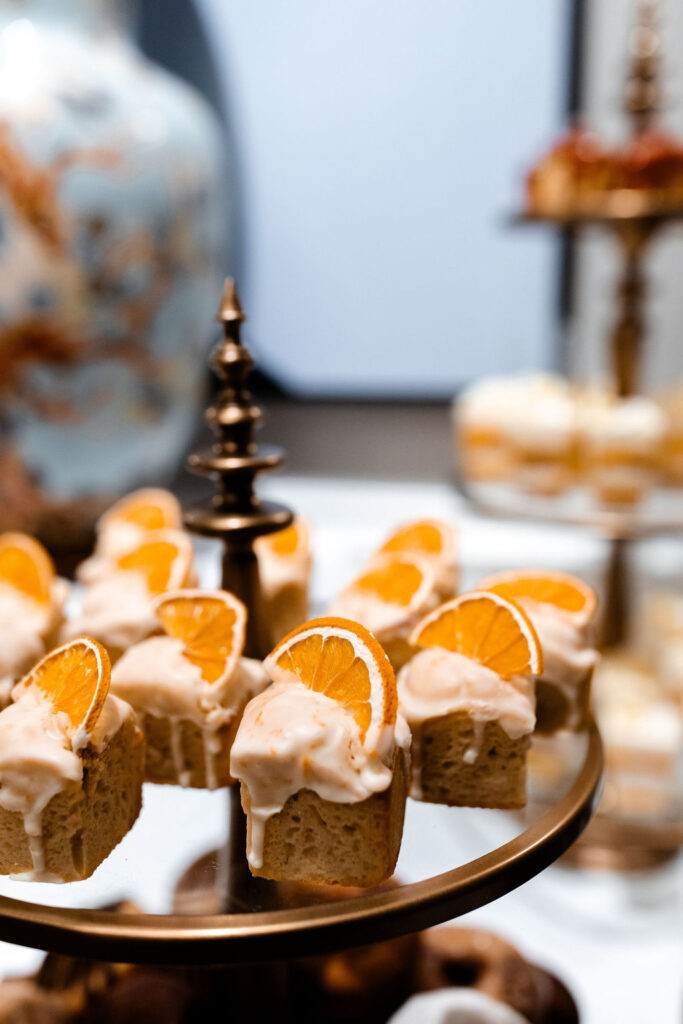 Close-up of mini orange-glazed cakes topped with dried orange slices on a tiered stand.
