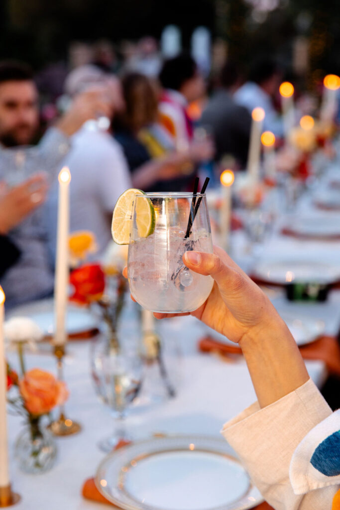 Guest holding up a cocktail with lime garnish for a toast at the reception table.