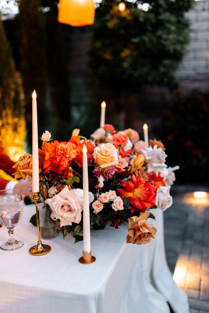 Sweetheart table decorated with taper candles and orange-toned floral centerpieces at Mid Century Manor.