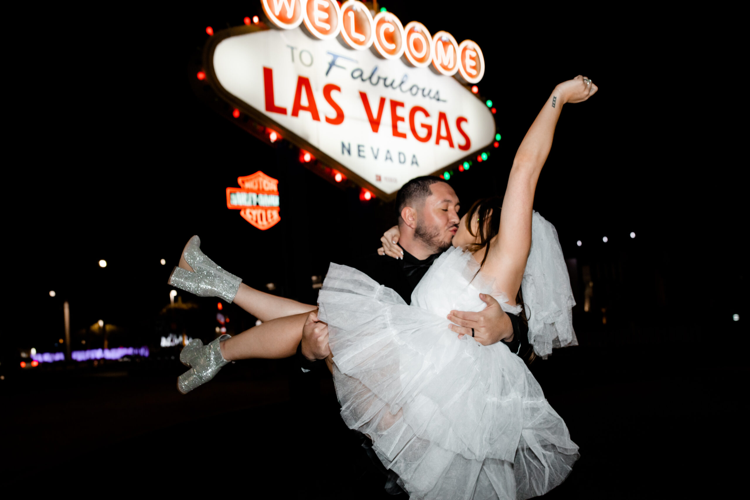 Groom picking up and kissing his bride during their nighttime Las Vegas elopement photos at the Welcome to Fabulous Las Vegas sign