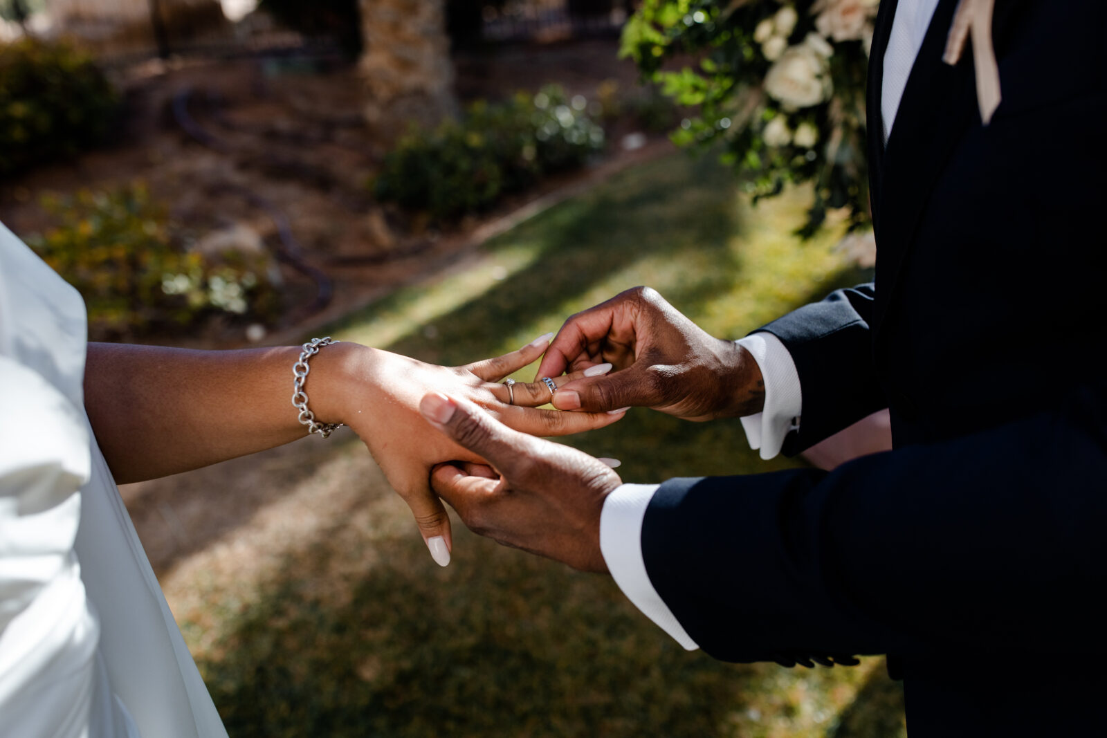 Groom placing the ring on his brides hand during their outdoor wedding ceremony